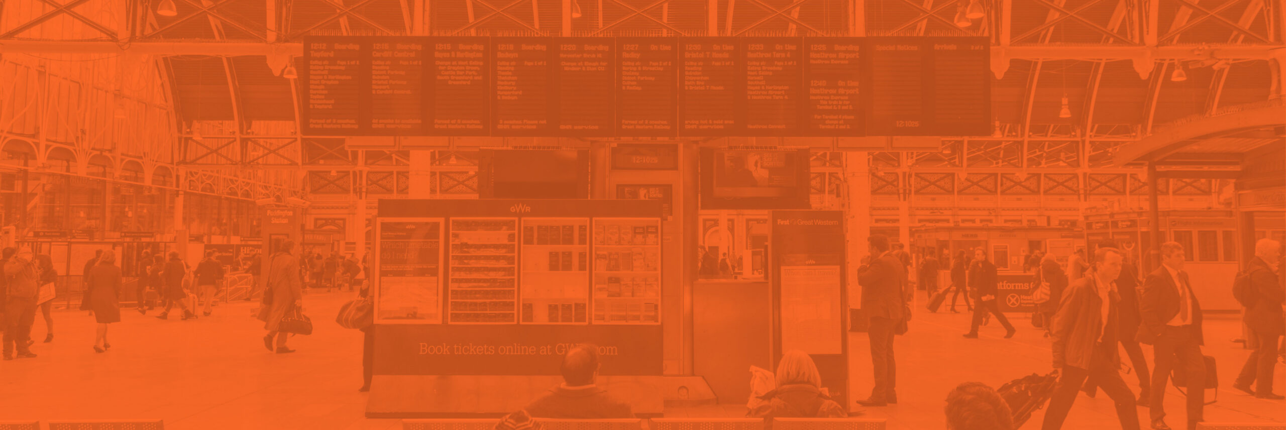 An electronic passenger information board inside a busy train station giving passengers information about destinations, departures, arrivals, delays, timings and platform numbers with a digital clock.